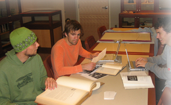 Spencer Power, Alex Hoselton, and Alex Ubbelohde sitting at a table in the library working on a paper.