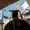 A person wearing a cap and gown is in silhouette in front of downtown Minneapolis buildings